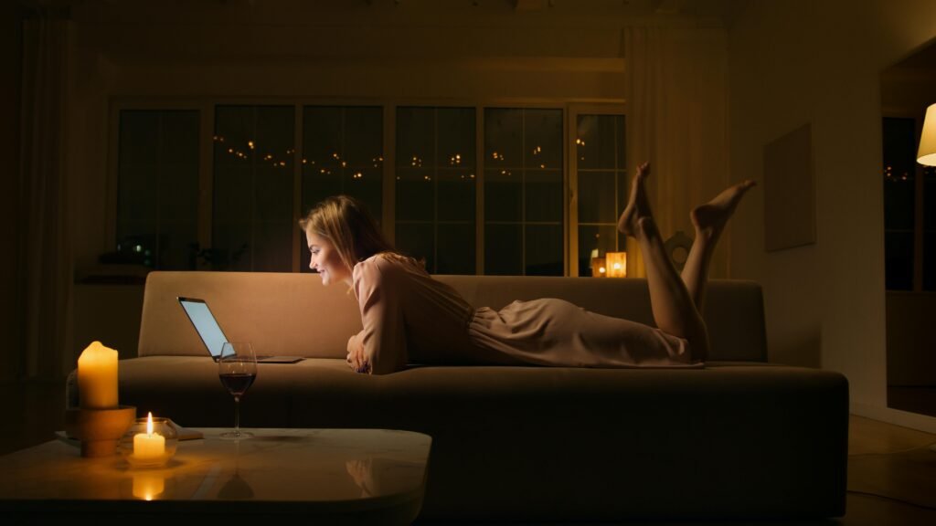 Caucasian woman smiling and relaxing on a sofa with a laptop at night.